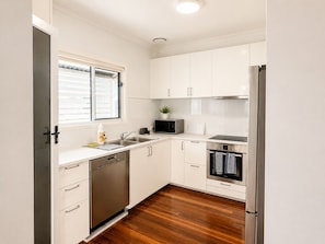 A compact kitchen with white cabinets, a stainless steel refrigerator, a dishwasher, and a microwave. - Charming Queenslander 3 bed 1 bath in West End (West End)