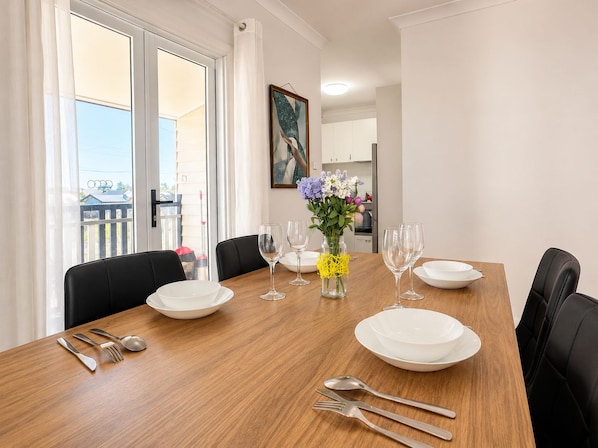 A dining table set with white plates, cutlery, and wine glasses, with a vase of flowers in the center. - Charming Queenslander 3 bed 1 bath in West End (West End)