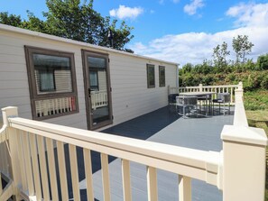Eine überdachte Terrasse mit Tisch und Stühlen, einem weißen Geländer und einer Tür mit Fenster.