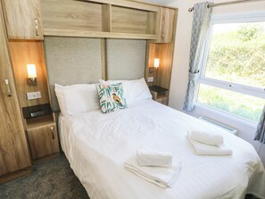Ein Hotelzimmer mit einem Bett, Kissen, einem Nachttisch, einer Lampe, einem Fenster mit Vorhängen und einer Heizung.
