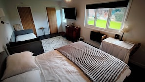 Un dormitorio con cama, cómoda, televisor y ventana con vista al exterior.