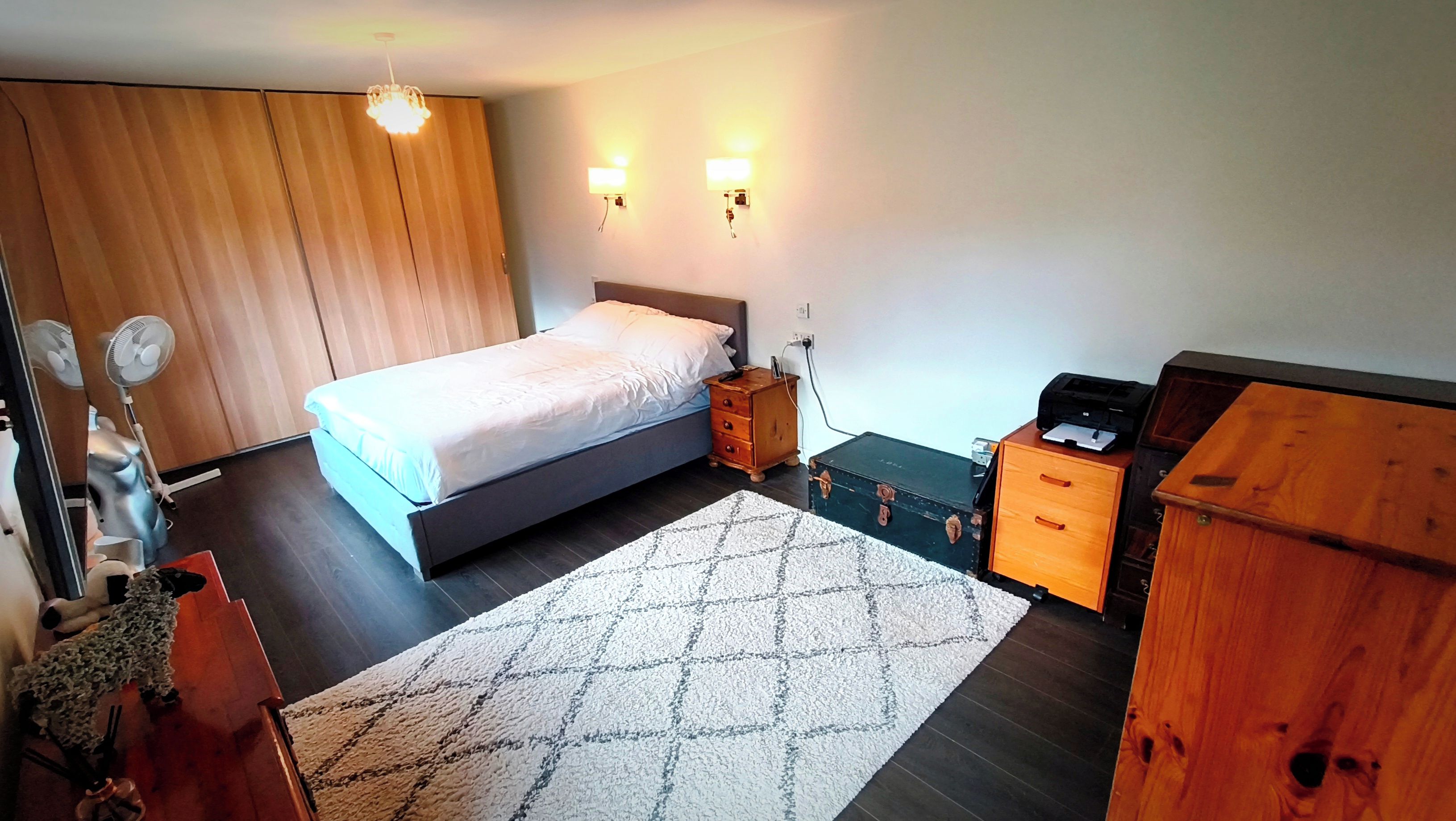 A bedroom with a bed, bedside table, dresser, and a rug.
