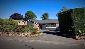 A residential house with a paved driveway, a stone wall, and a well-maintained hedge.