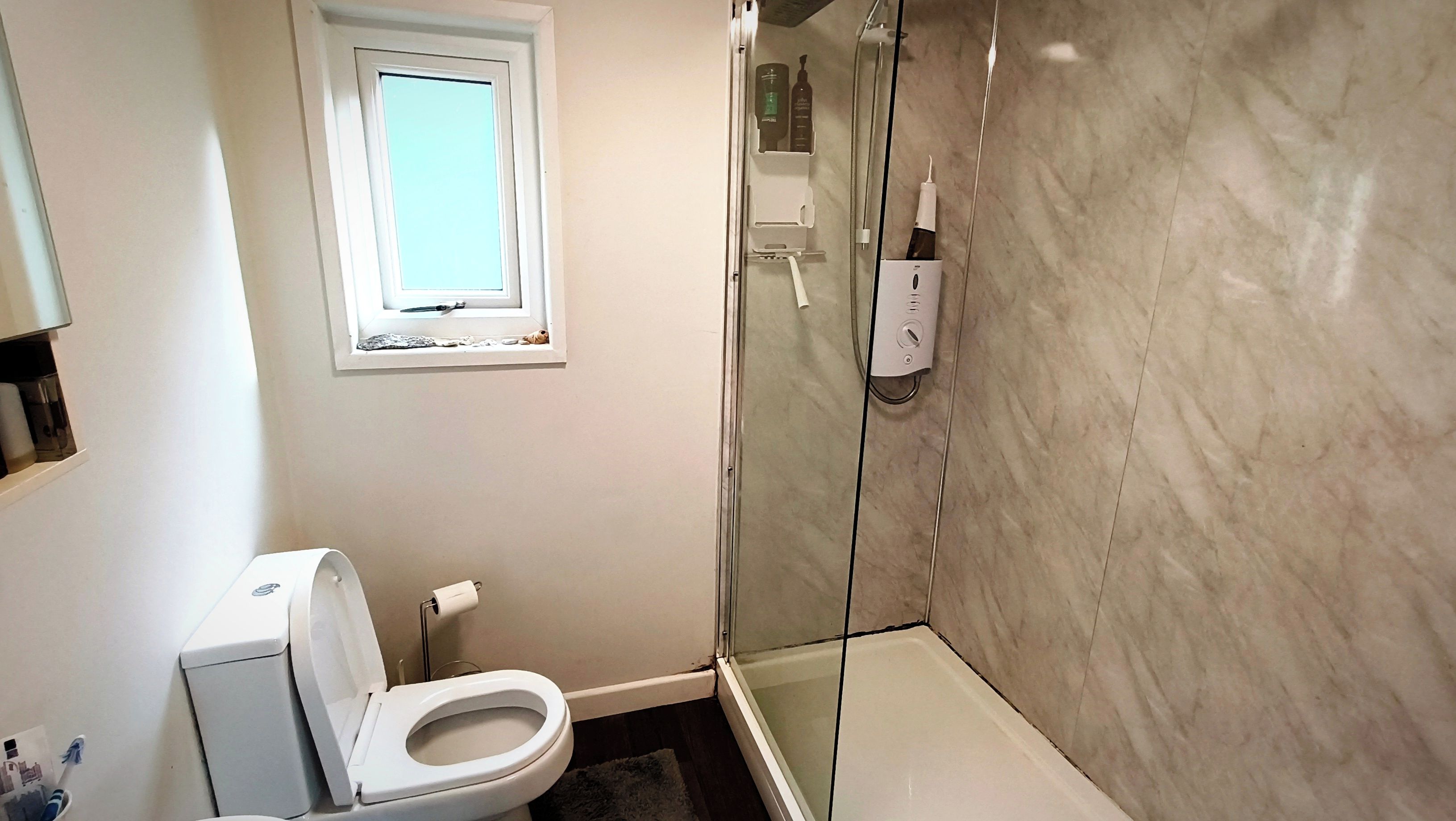 A bathroom with a toilet, a shower, and a window.