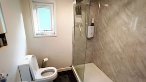 A bathroom with a toilet, a shower, and a window.