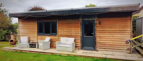 Una cabaña de madera con dos sillones de mimbre, una mesa pequeña, una puerta y una ventana.