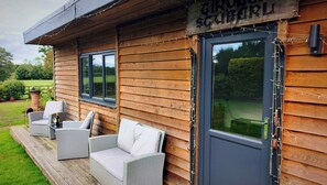 A wooden cabin with a deck, wicker furniture, and a sign reading 'CIRROBER SCHUBERL'.
