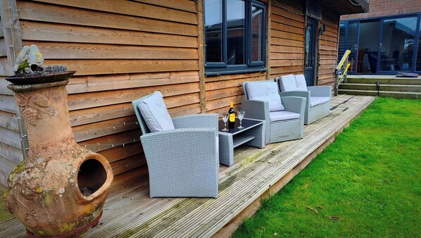 A wooden deck with wicker furniture and a wine bottle.
