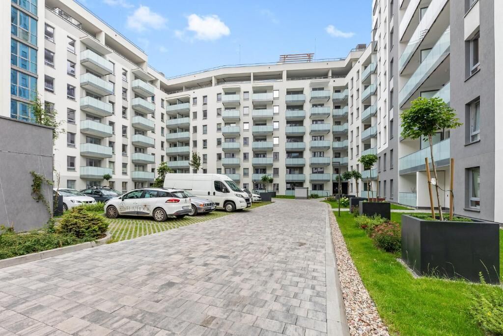 Un immeuble d’appartements moderne doté de nombreux balcons, d’une allée pavée et de véhicules stationnés.