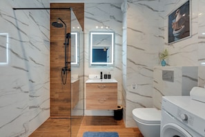 A modern bathroom with a glass-enclosed shower, wooden vanity, a toilet, and a washing machine. - Horizon - Gdansk Seaside (Gdańsk)