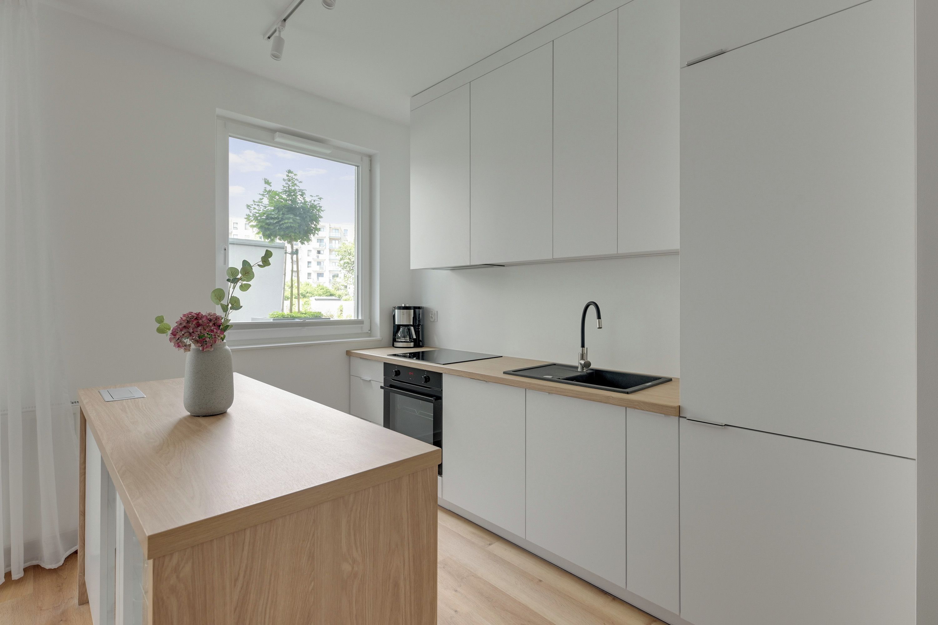 Una cocina moderna con encimera de madera, un fregadero y una ventana con vistas a edificios y árboles.