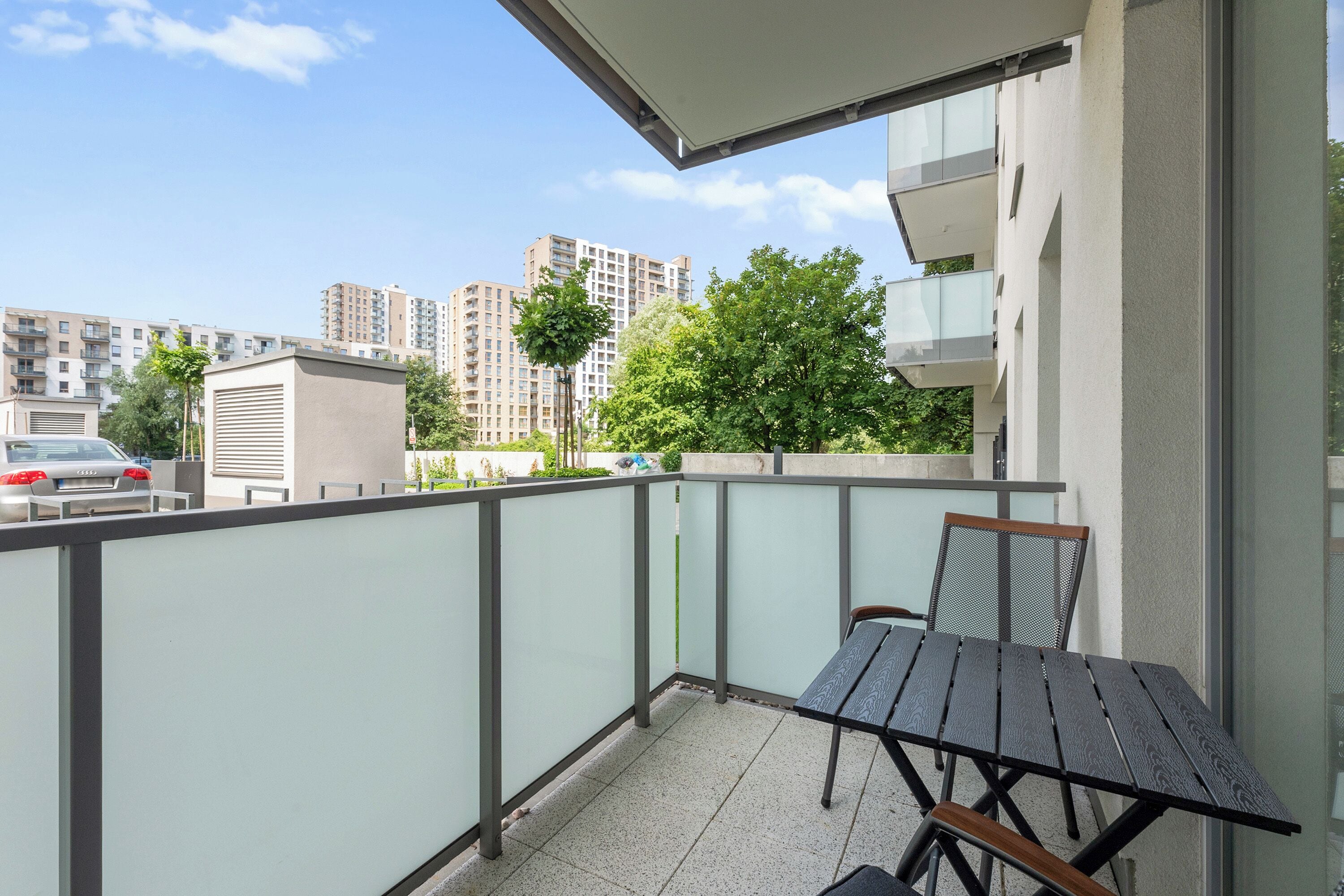 Un balcon avec une table et des chaises, une vue sur un paysage urbain avec des immeubles et un ciel dégagé.