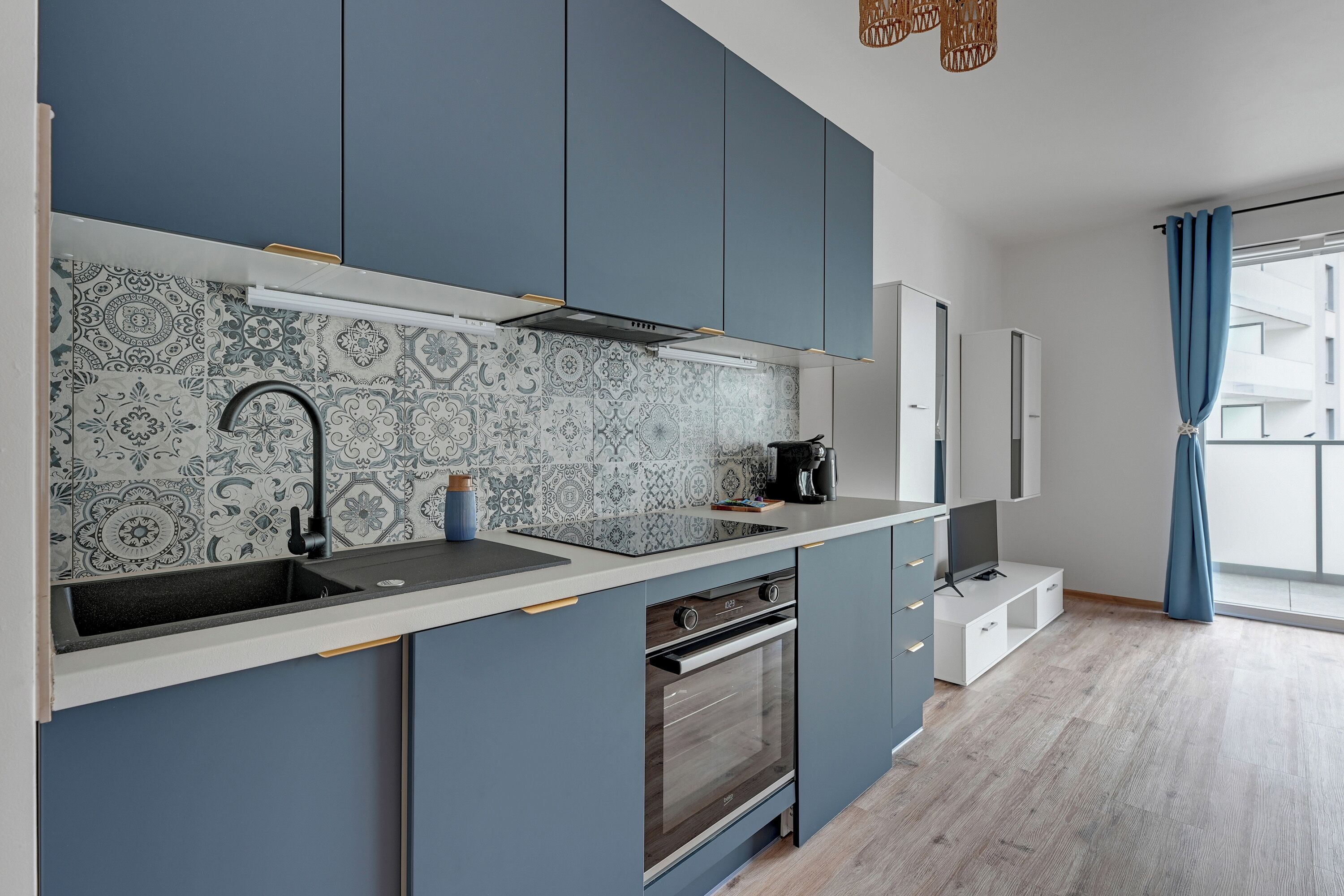 Una cocina moderna con armarios azules, un salpicadero estampado y un horno empotrado.