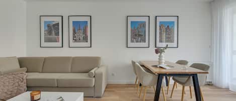 Una sala moderna con un sofá, una mesa de comedor con sillas y tres cuadros en la pared.