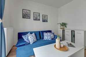 A modern living room with a blue sofa, decorative pillows, a white coffee table, and wall art depicting nautical themes. - Horizon - Gdansk Seaside (Gdańsk)