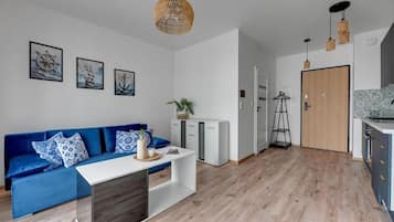 A modern living space with a blue sofa, white console table, and a kitchen area with a wooden door.
