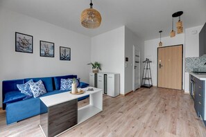 Un espacio de estar moderno con un sofá azul, una consola blanca y una zona de cocina con puerta de madera.