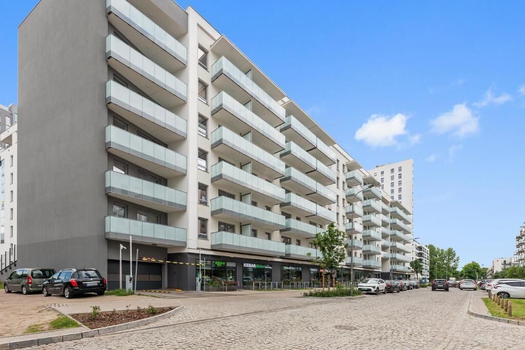 Edifício residencial de vários andares com varandas, um pátio pavimentado e carros estacionados.