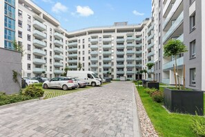 A modern apartment building with a central courtyard, a paved walkway, and a parking area with cars and a van. - Horizon - Gdansk Seaside (Gdańsk)