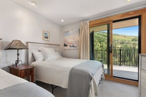 Ein Schlafzimmer mit einem Bett, einem Nachttisch, einer Lampe, einem Gemälde und einem Balkon mit Blick auf eine gebirgige Landschaft.