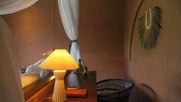 A room with a bed, a bedside table with a lamp, a chair, and a decorative wall hanging.
