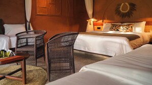 A hotel room with two beds, a sitting area with wicker furniture, and a wall-mounted lamp. - Giraffe Manor Tanzania (Arusha)
