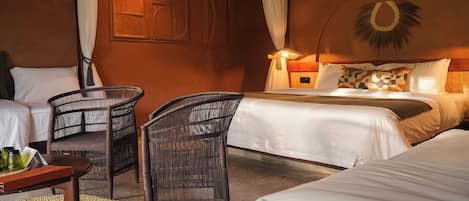 A hotel room with two beds, a sitting area with wicker furniture, and a wall-mounted lamp.