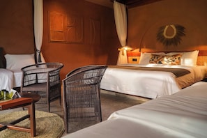 Habitación de hotel con dos camas, una sala de estar con muebles de mimbre y una lámpara fijada a la pared.