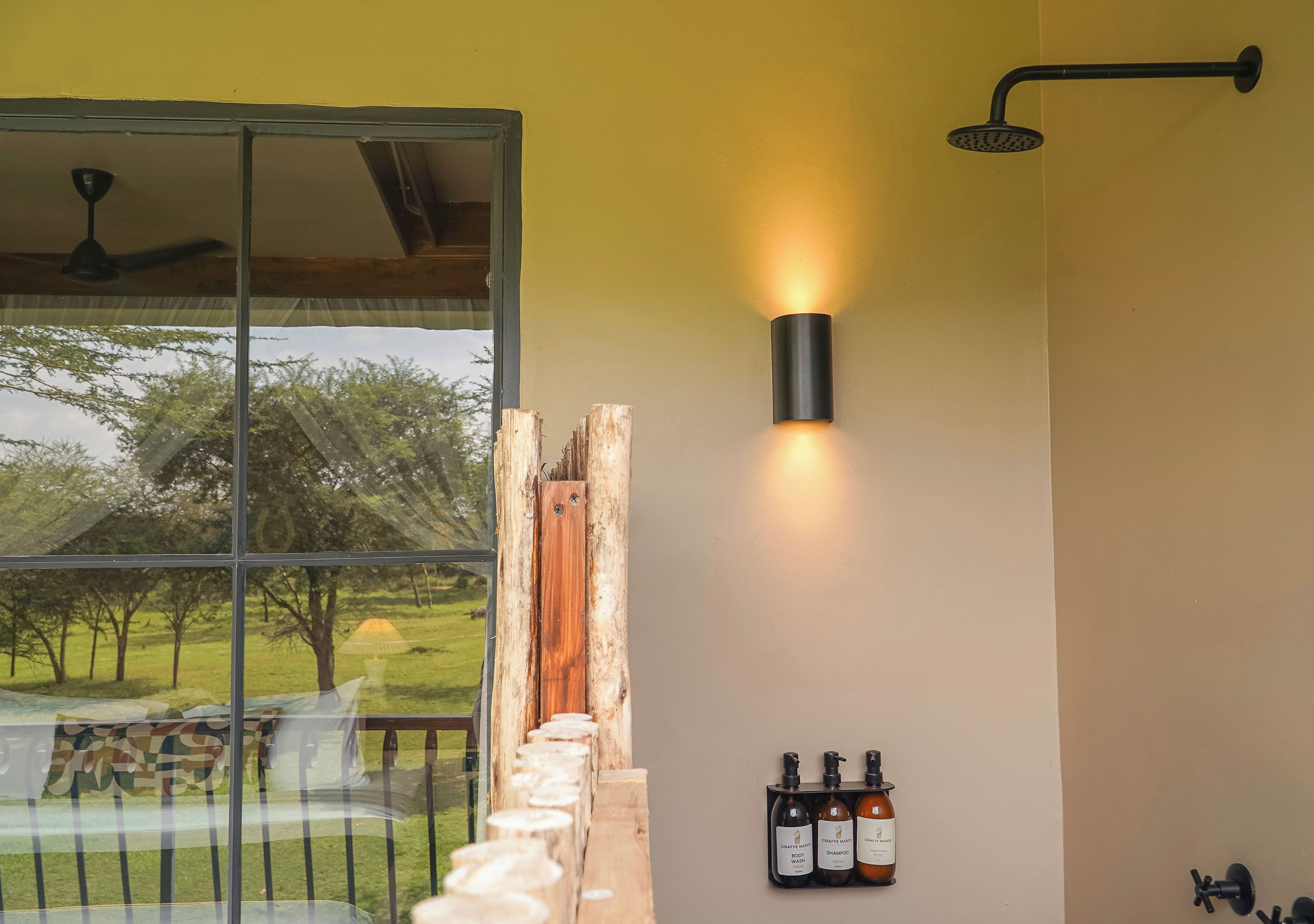 A bathroom with a shower, a wall-mounted light, and a window with a view of trees.