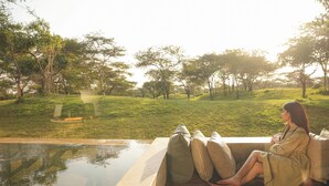 A person sitting by a pool with a view of a grassy landscape and trees. - Giraffe Manor Tanzania (Arusha)
