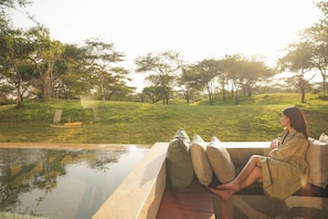 Una persona sentada junto a una piscina con vista a un paisaje con césped y árboles.