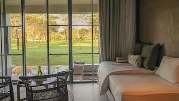 A room with a bed, a table with chairs, and a view of a grassy area through large windows.