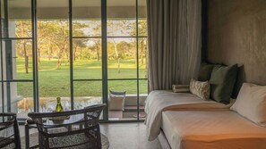 Una habitación con una cama, una mesa con sillas y vistas a un área verde a través de ventanas amplias.