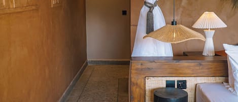 A hotel room with a bed, a nightstand, a lamp, a woven mat, and a wall with a decorative panel.