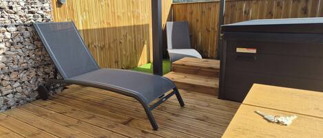 Una terraza de madera con una tumbona, un jacuzzi y un muro de piedra.