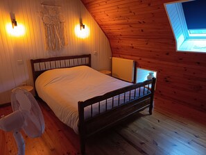 Ein Schlafzimmer mit einem hölzernen Bett, einem Standventilator und einem Oberlicht.