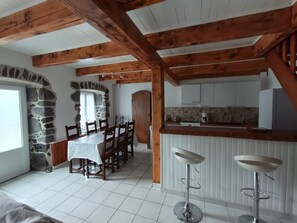 Uma área de refeições com mesa e cadeiras, uma cozinha com armários brancos e uma parede de pedra.