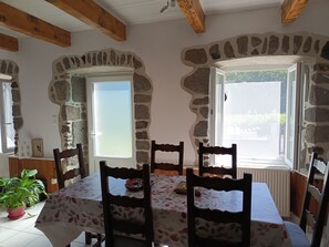 Ein Essbereich mit einem für vier Personen gedeckten Tisch, umgeben von Steinwänden und Holzbalken, mit Blick ins Freie durch ein Fenster.