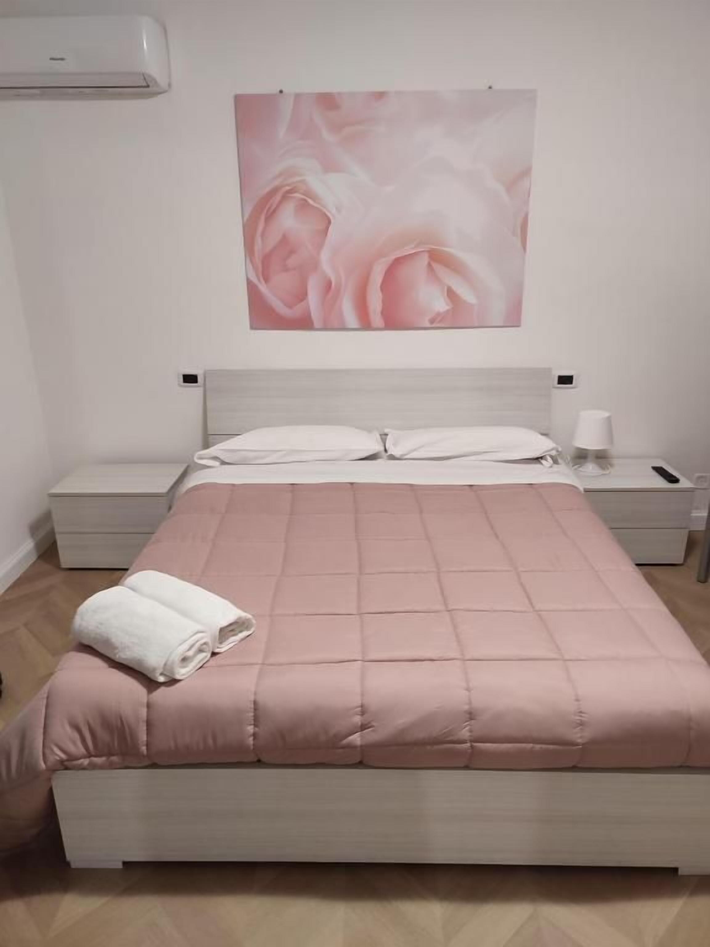 A bedroom with a bed, a nightstand, a wall-mounted air conditioner, and a framed picture on the wall.