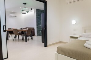 A modern hotel room with a bed, bedside table, and a dining area with chairs and a table. - Villa delle Rose Pompei Room and Suite (Pompei)