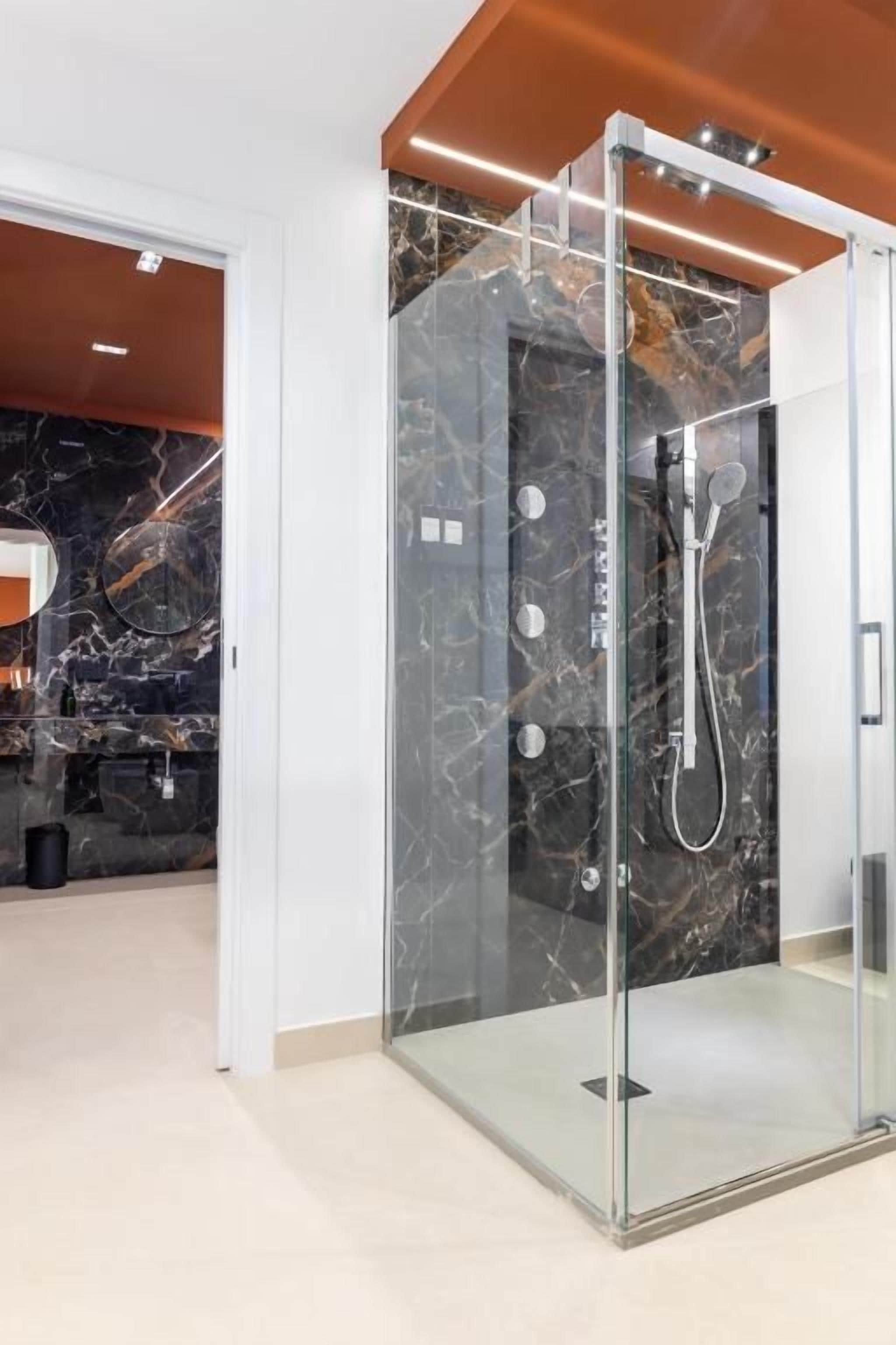 Un baño moderno con ducha de vidrio, paredes de mármol y una zona de lavamanos visible.