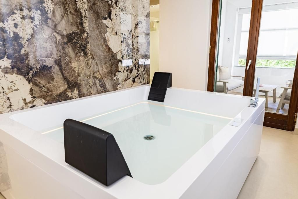 A modern bathroom with a large bathtub, a marble wall, and a view of an outdoor seating area.