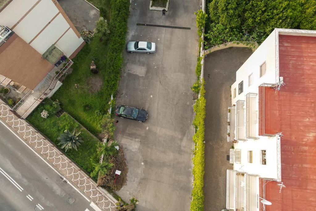 Vista aérea de una calle residencial con dos coches estacionados a un lado, una senda peatonal y un edificio con techo rojo.
