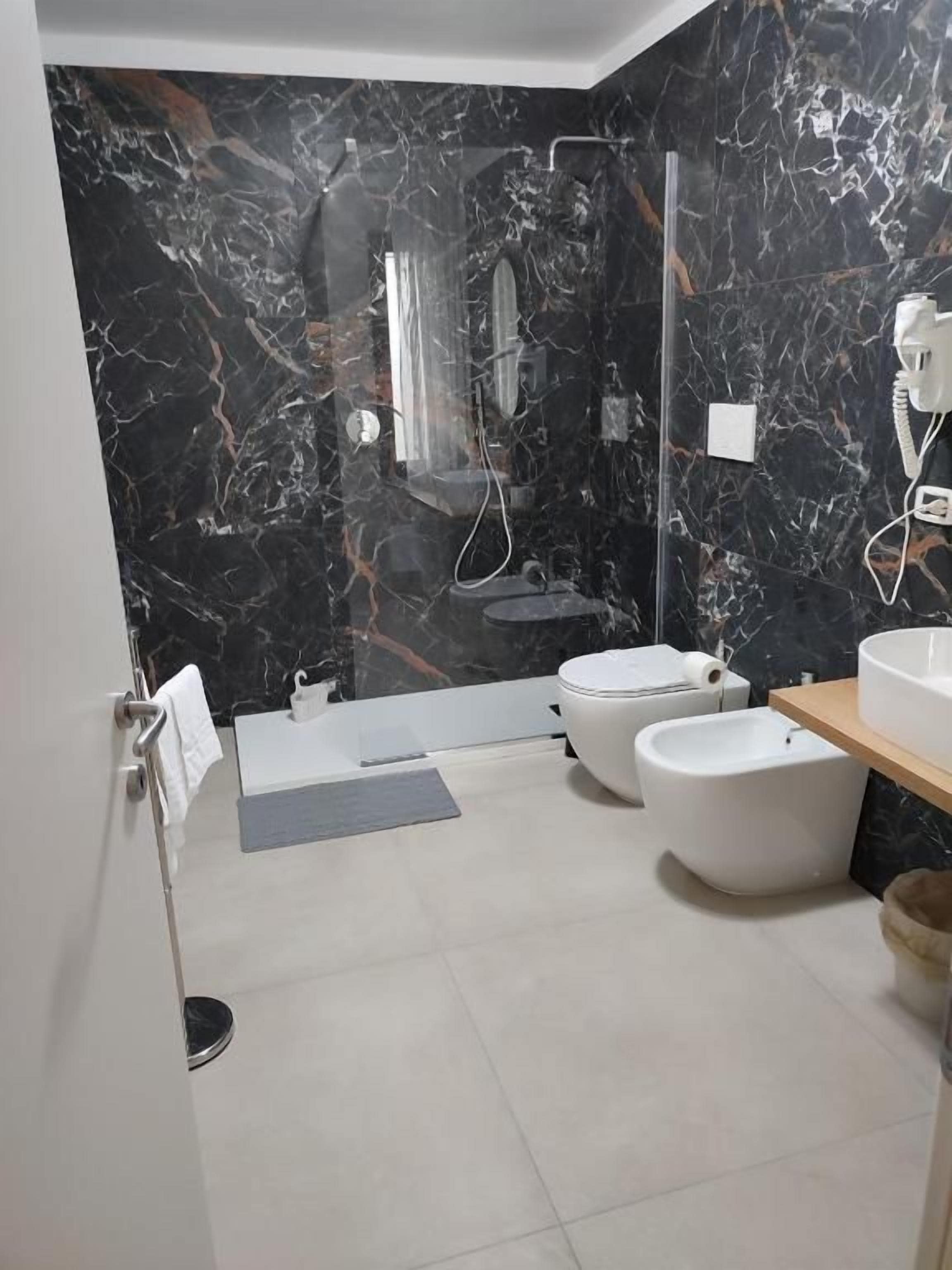 A modern bathroom with a marble wall, a bathtub, a toilet, and a shower area.