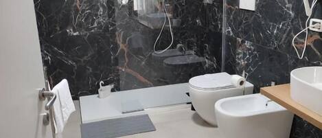 A modern bathroom with a marble wall, a bathtub, a toilet, and a shower area.