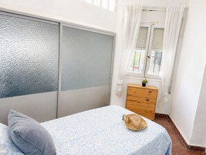 Ein Schlafzimmer mit einem Bett, einer Holzkommode, einem Fenster mit Vorhängen und einer Wand mit Strukturpaneelen.