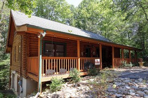 Eine Blockhütte mit Veranda, einem Schild, das sie als Bärenlodge kennzeichnet, und einer Steinsitzbank.