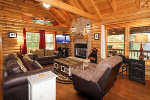 A log cabin interior with a fireplace, a television, a sofa, and a bear statue. - Hot tub, pet friendly, pool table, 5 bedroom near downtown Gatlinburg! (Gatlinburg)