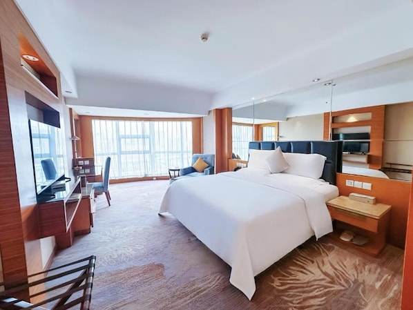 A hotel room with a large bed, a desk, a chair, and a TV.