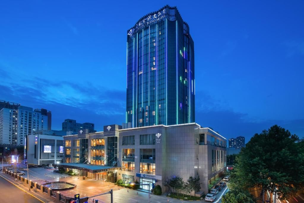 A modern hotel with a prominent tower, multiple entry points, and a well-lit parking area.